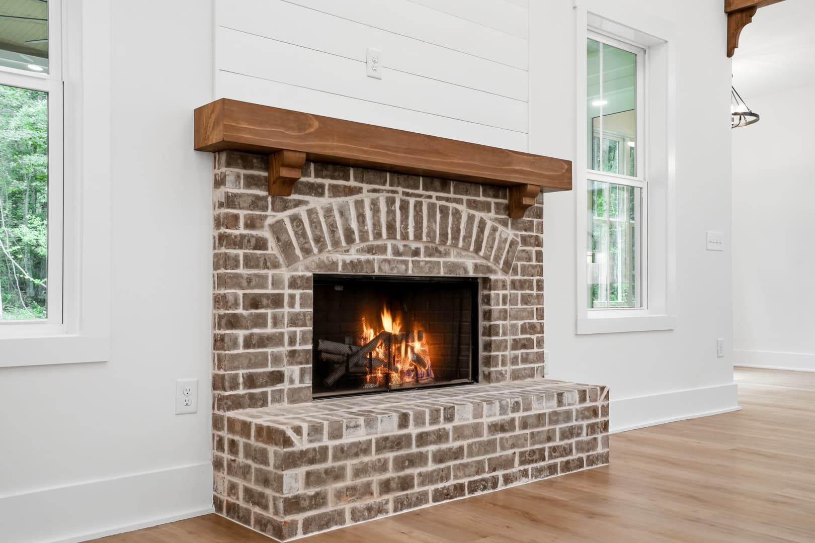 Weathered brick fireplace with a thick wood mantle and a warm fire burning inside.