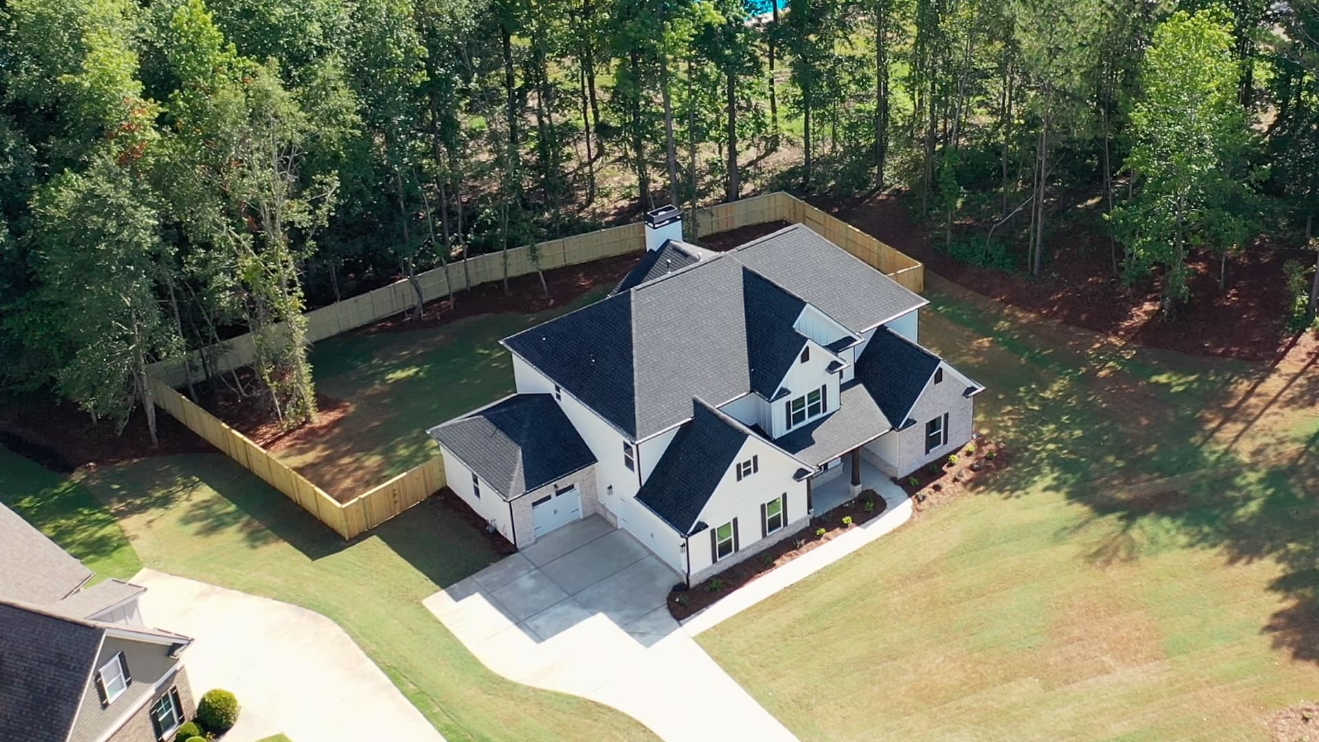 Aerial view of a modern white two-story house with black roof and fenced backyard.