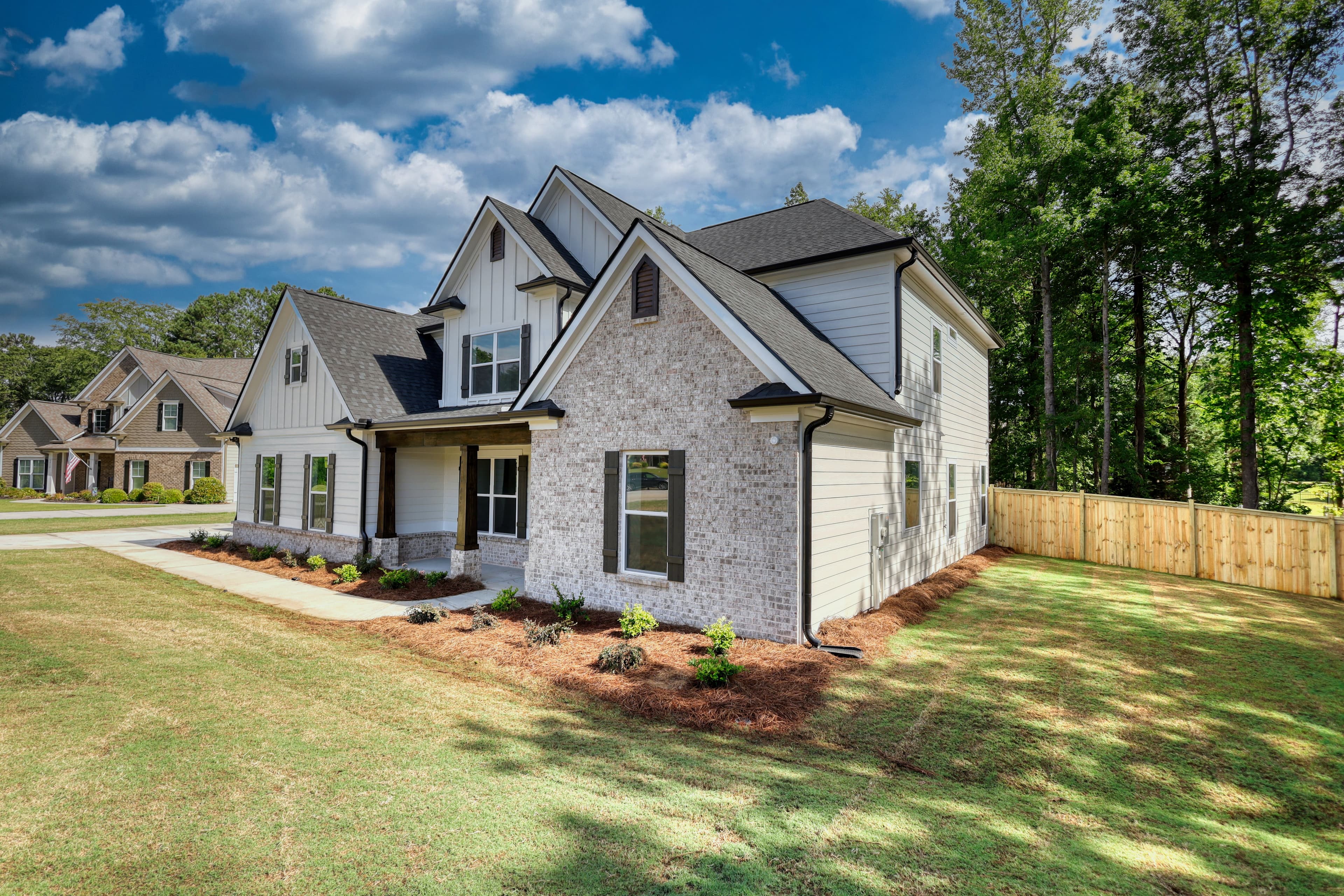 Modern two-story house with white board and batten siding, grey brick, and dark gabled roofs.