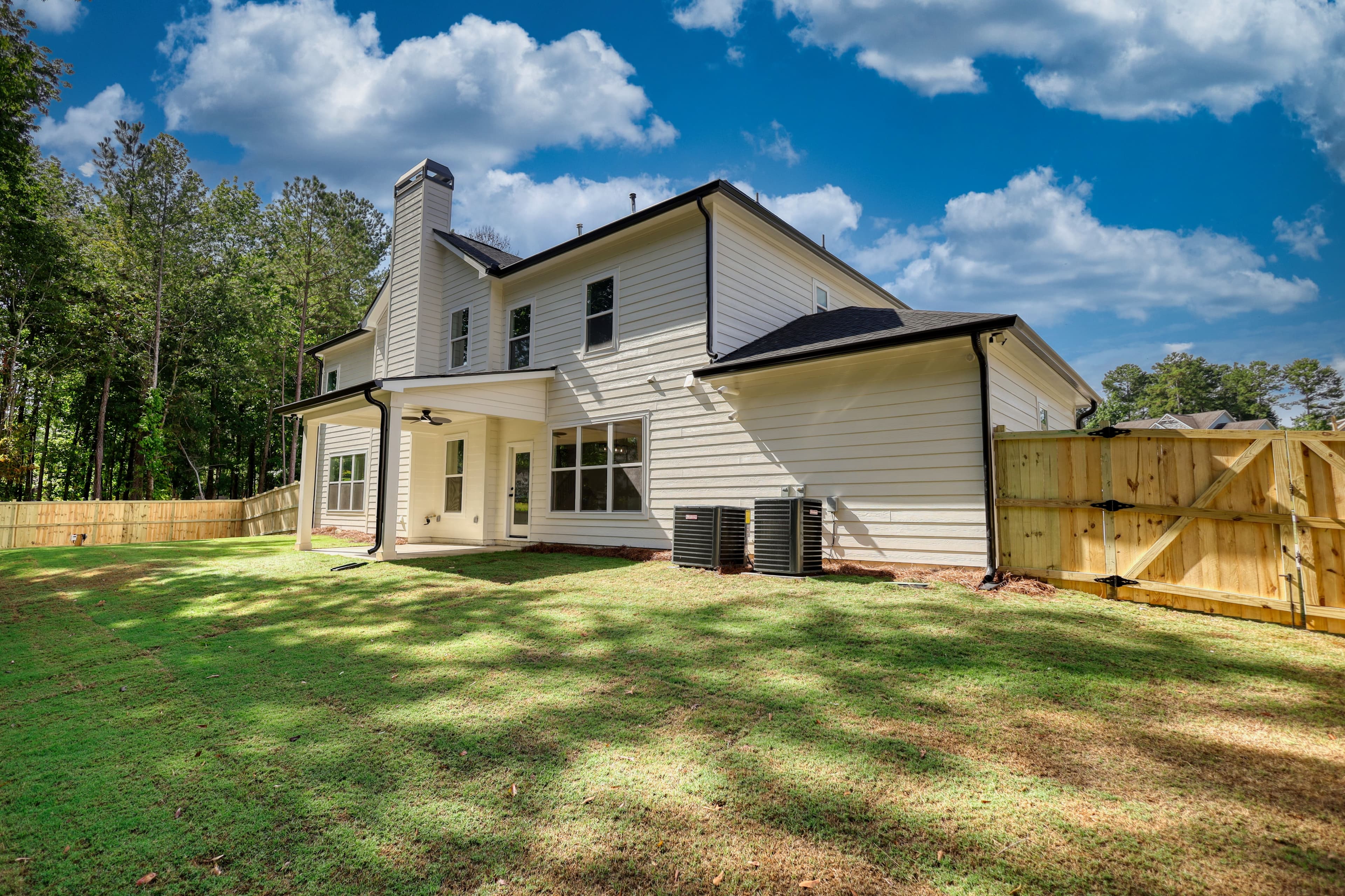 Back of a white two-story house with a covered patio, green lawn, and wooden fence.