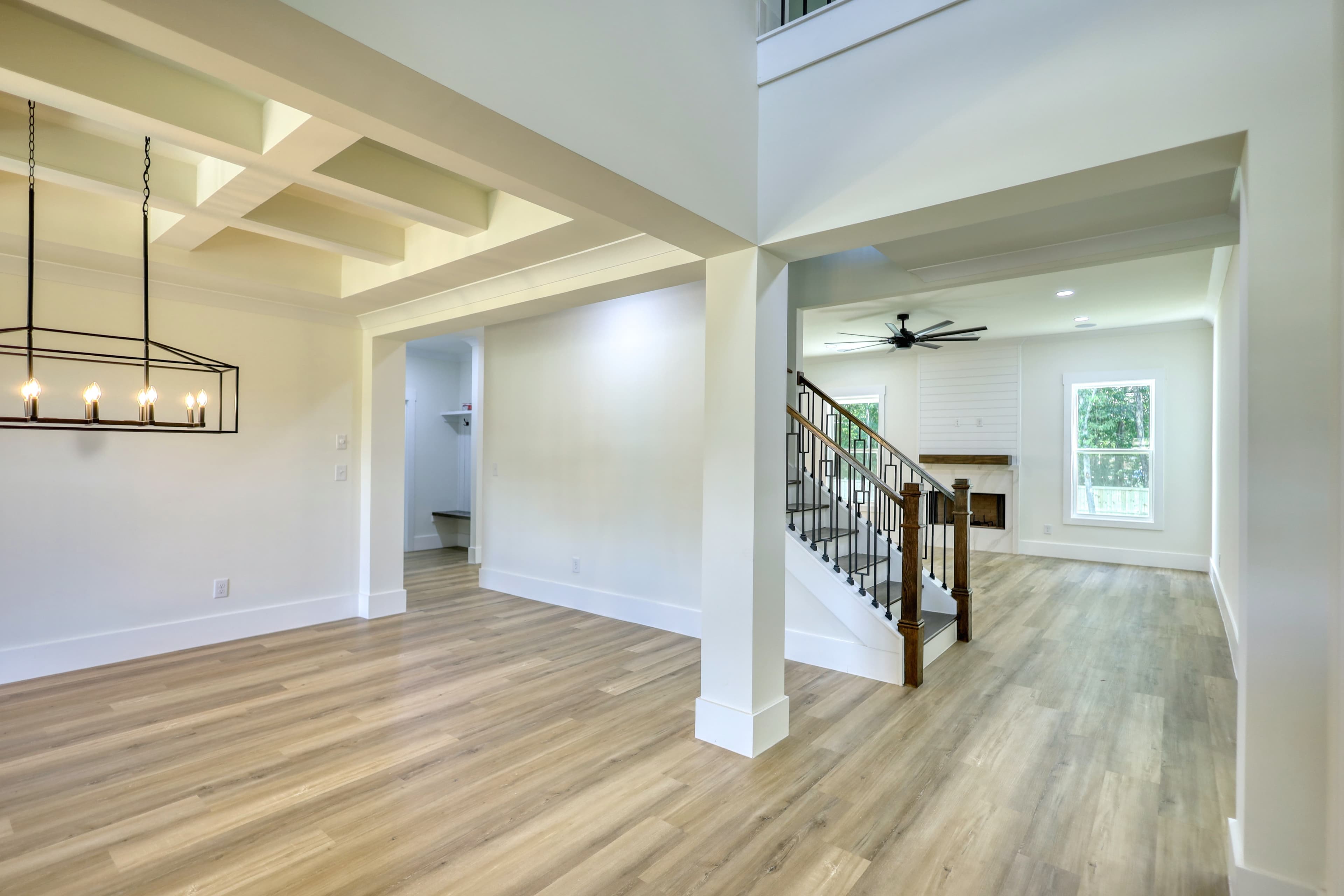Modern open-concept home interior with light wood floors, coffered ceilings, and a wooden staircase.