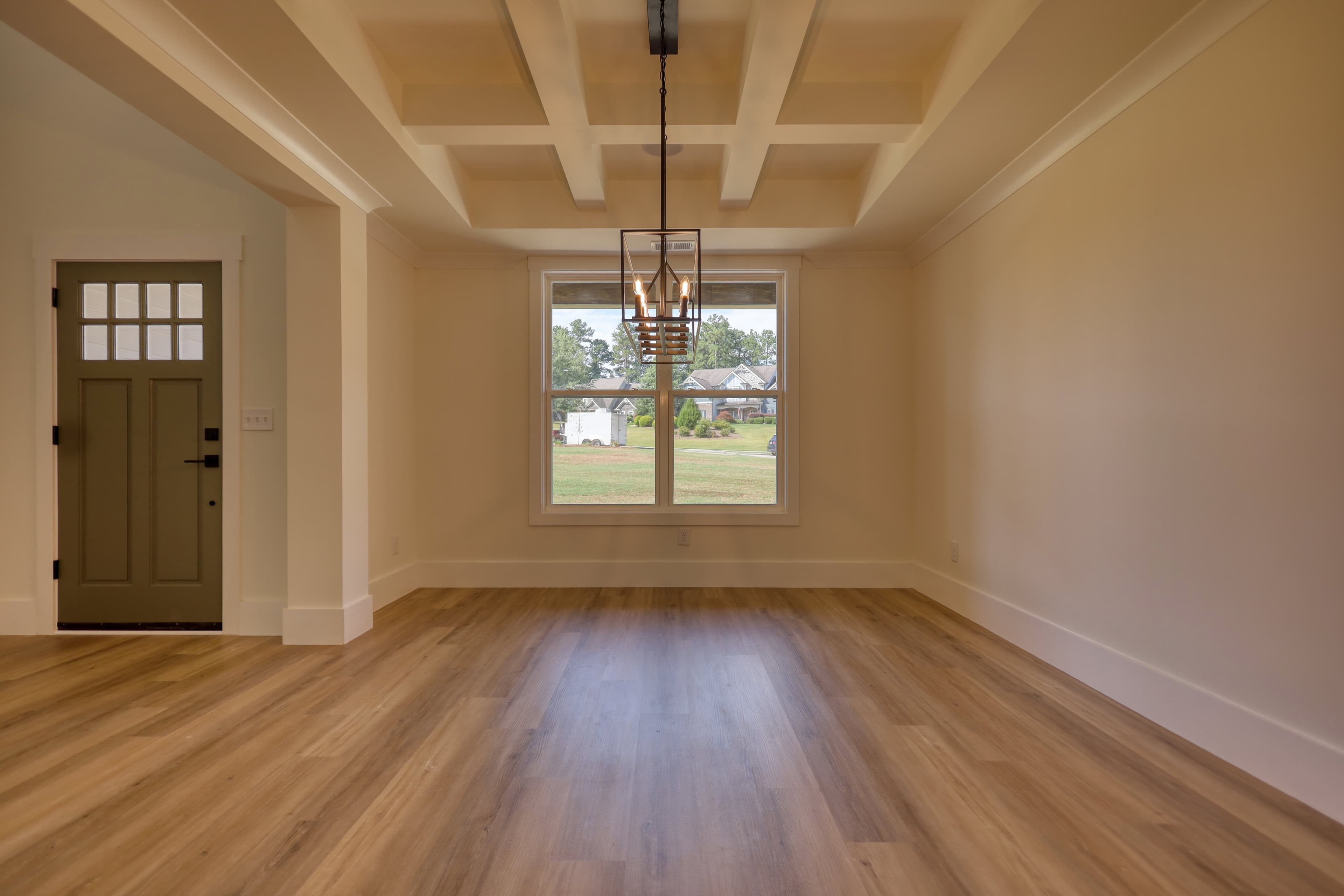 Empty room with light wood floors, a coffered ceiling, and a modern lantern chandelier.