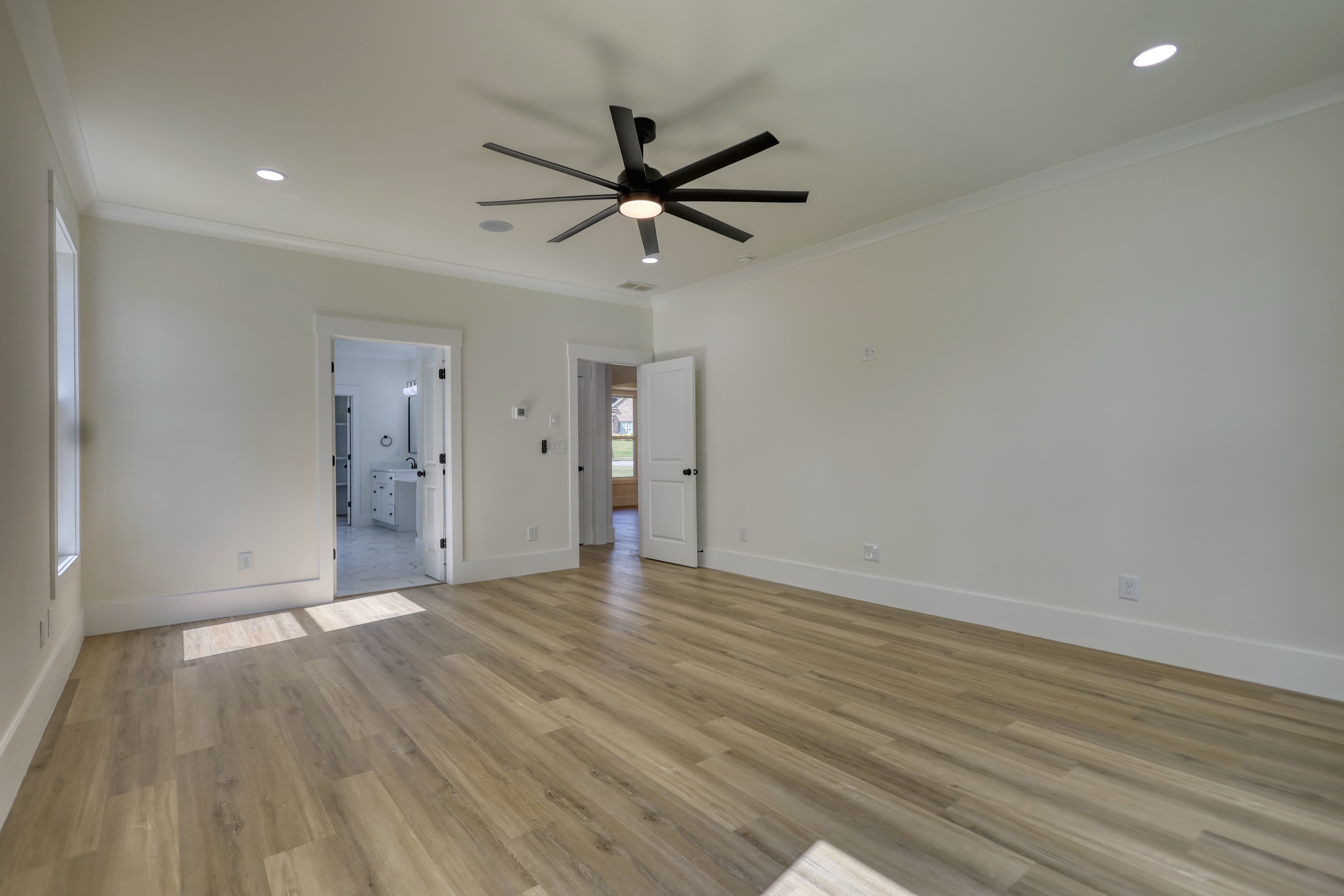 Empty room with light wood floors, white walls, and a large modern black ceiling fan.