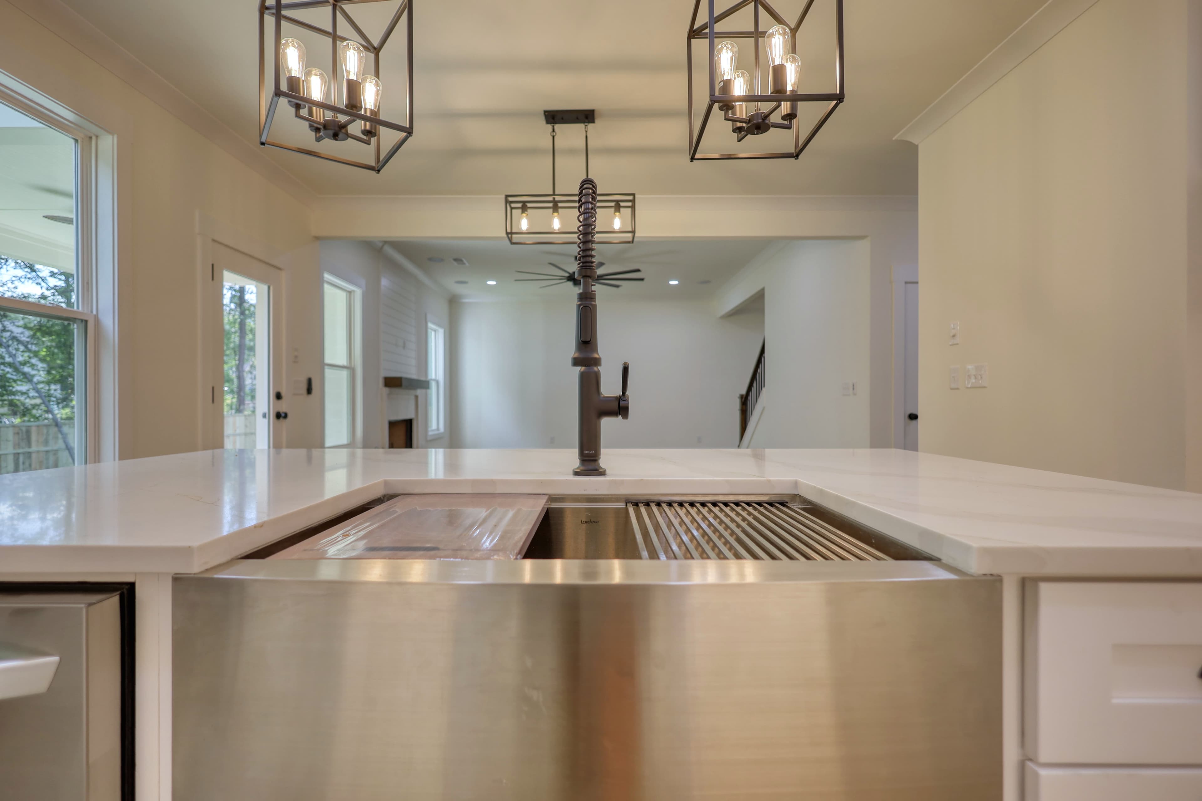 Stainless steel farmhouse sink on white marble countertop with black faucet and cage pendant lights.