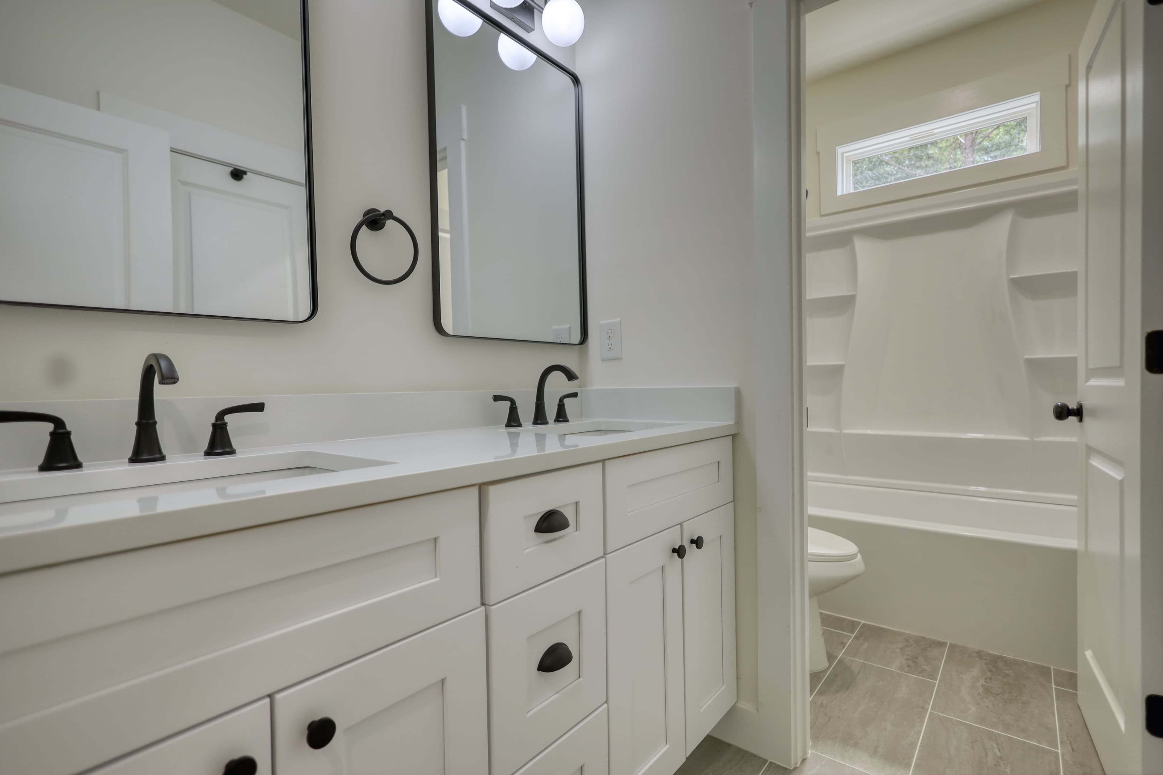 Modern white double vanity with black fixtures and mirrors, showing a separate bathtub area.