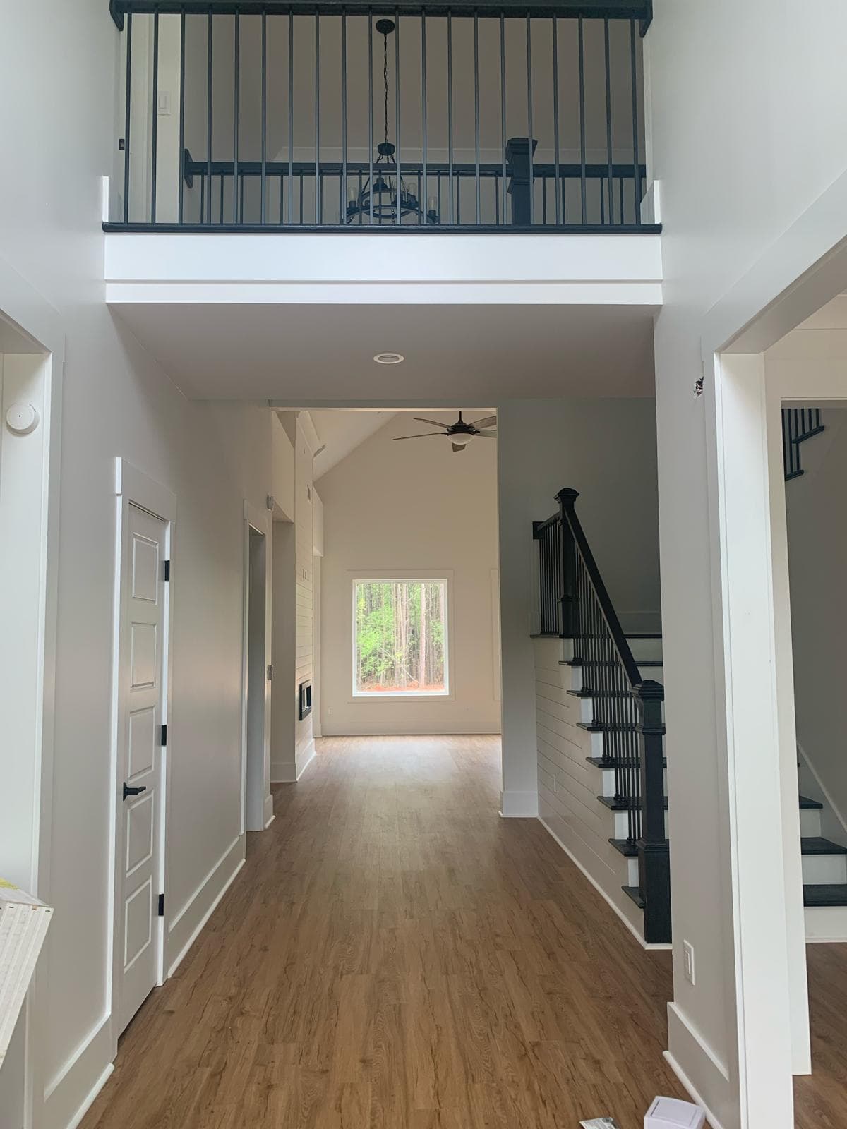Bright modern hallway featuring light wood floors, white walls, and elegant black metal railings.