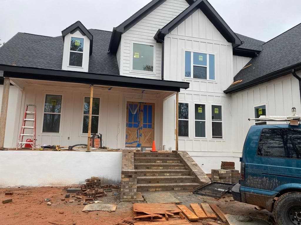 White farmhouse under construction with black trim, brick front steps, and a blue work van.