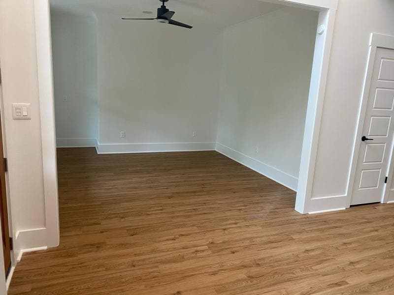 Empty room with light wood-look flooring, white walls, and a black ceiling fan overhead.