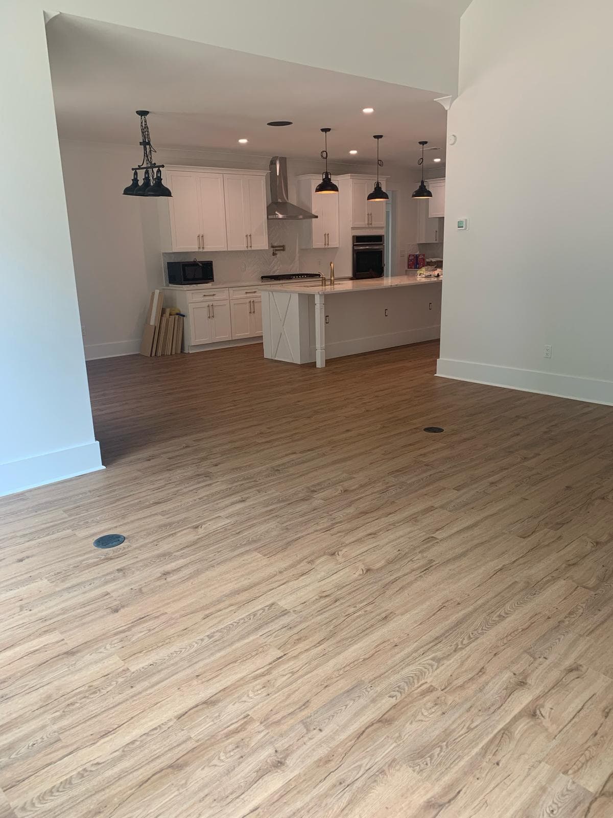 Modern open-concept kitchen with white cabinets, light wood flooring, and black industrial pendant lights.