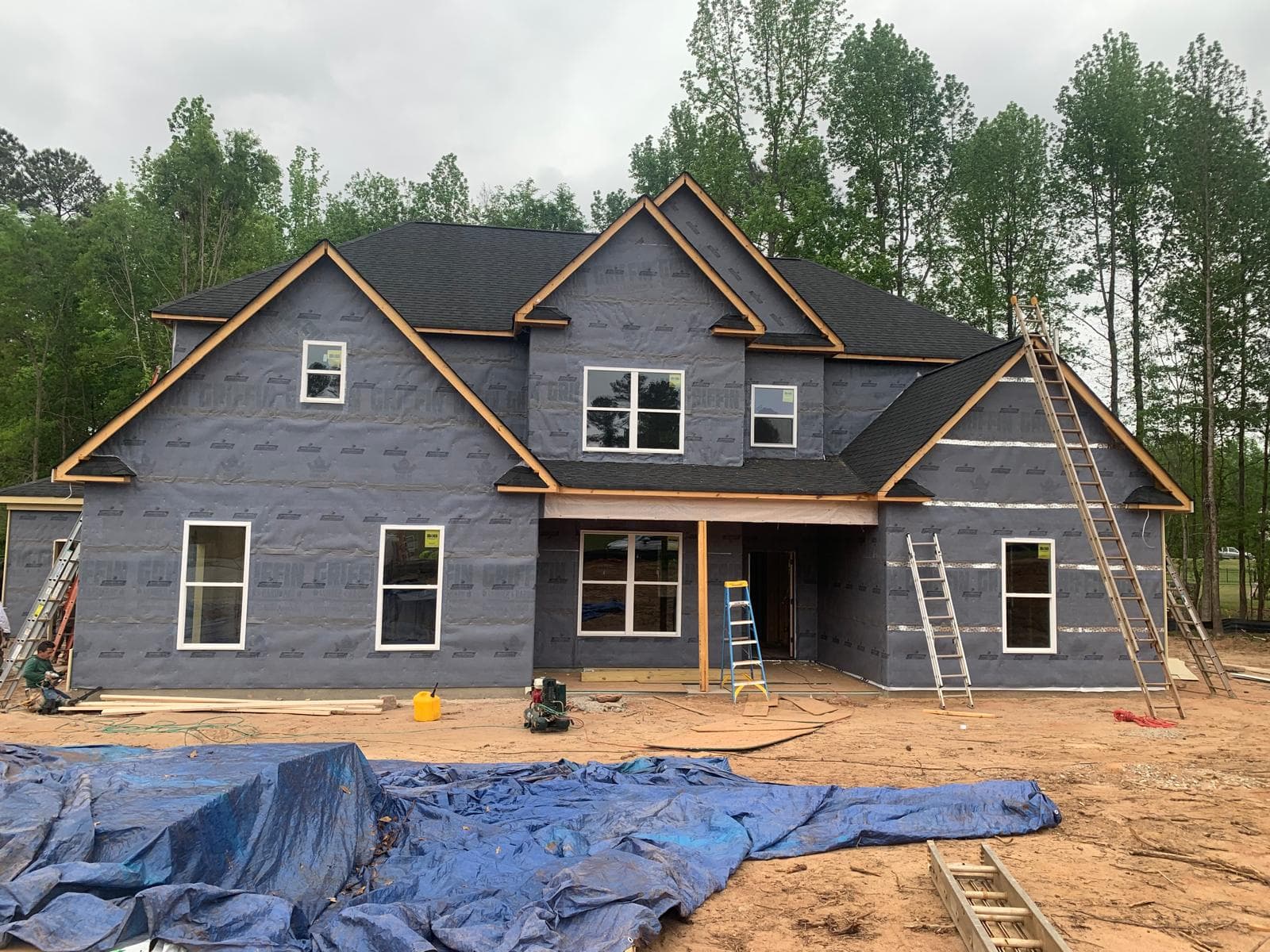 Large two-story house under construction with grey house wrap, black roof, and white windows.